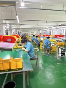 Workers assembling cables at individual workstations in a manufacturing facility.