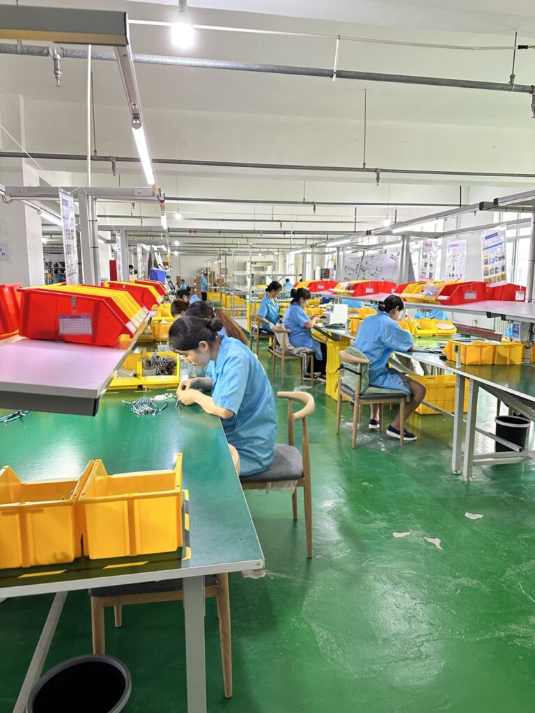 Workers assembling cables at individual workstations in a manufacturing facility.