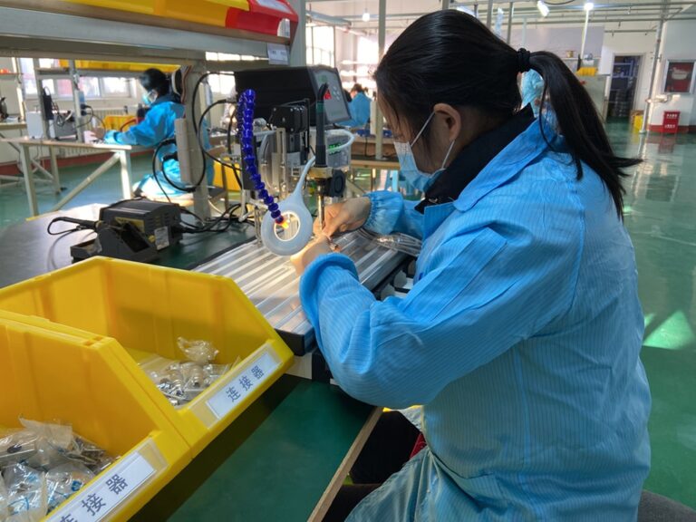 A worker in a blue uniform assembling wire harnesses at a manufacturing station.